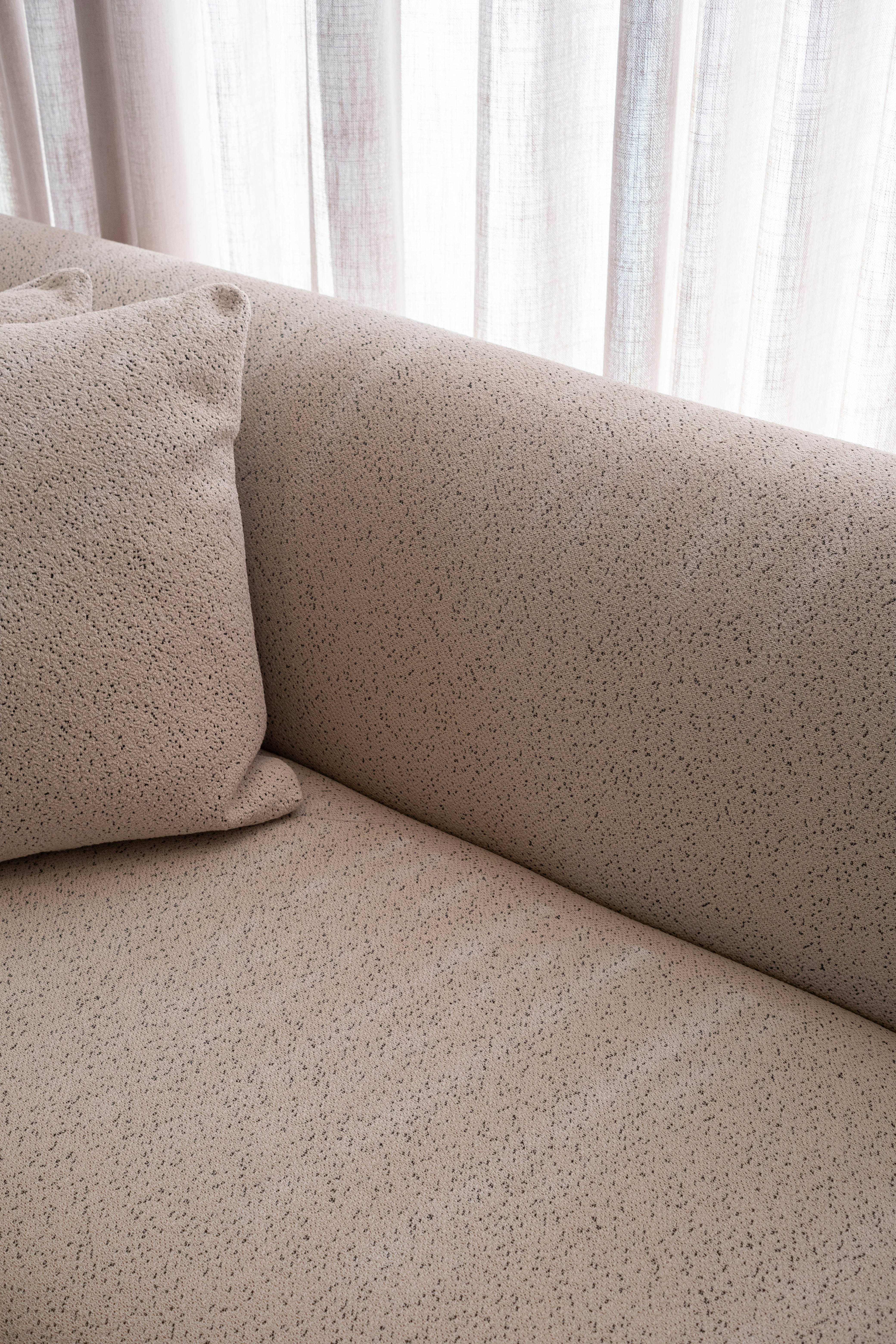 A textured beige sofa with a pillow and curtains.